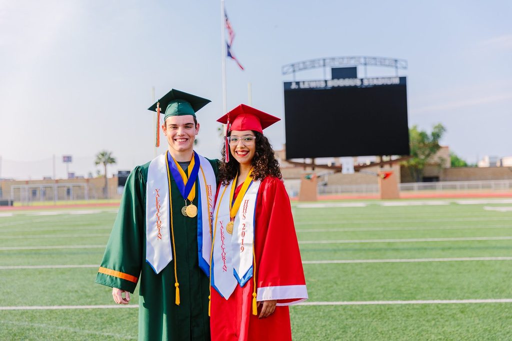Two HCISD graduates in caps and gowns on the field at Boggus Stadium